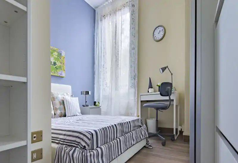 Bright, well-styled single bedroom with striped bedding, bedside table and a small desk by the window — ideal for a student or single occupant.