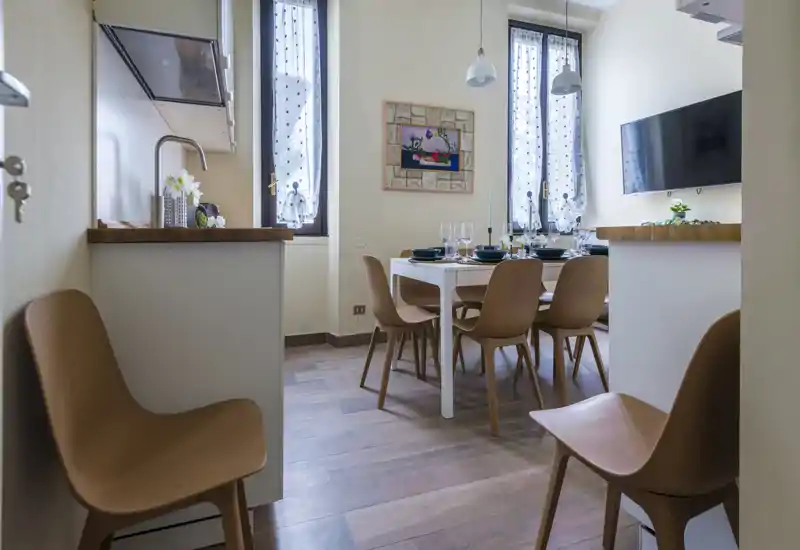 Bright, welcoming dining area with a set table for four, modern wooden chairs and natural light from tall windows—ideal for meals and small gatherings.