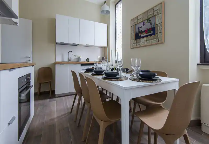 Bright and stylish dining area integrated with a compact kitchen, featuring a set table for six, modern cabinetry and warm wood-tone chairs — ideal for apartment listings.