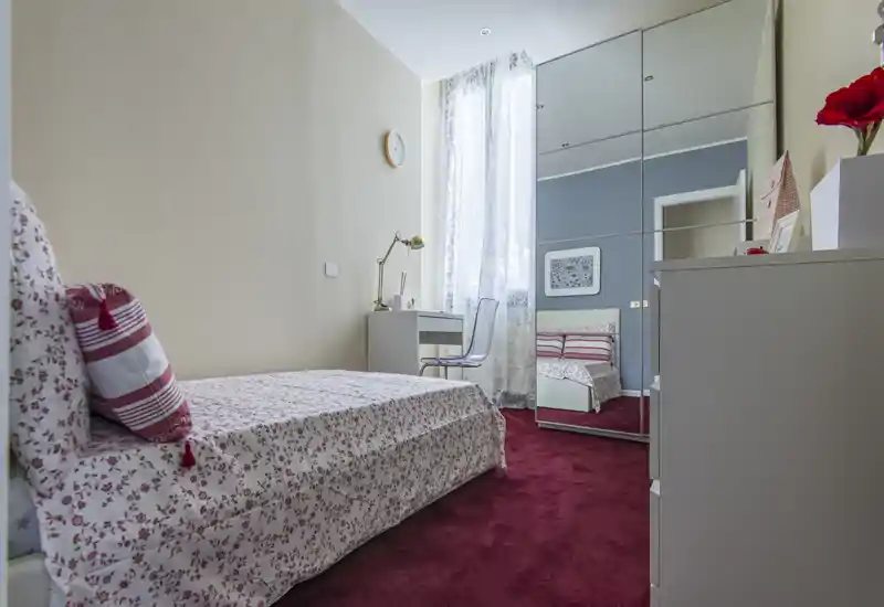 Accogliente camera singola con biancheria a fantasia, scrivania vicino alla finestra e armadio con ante a specchio che ampliano luce e spazio — perfetta per un soggiorno confortevole.
