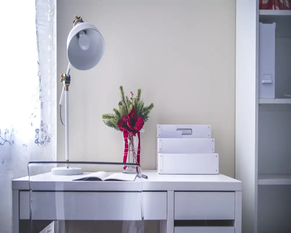 Small, bright bedroom workspace with a white desk, task lamp and decorative vase — clean, minimal styling ideal for a listing photo highlighting a study corner.