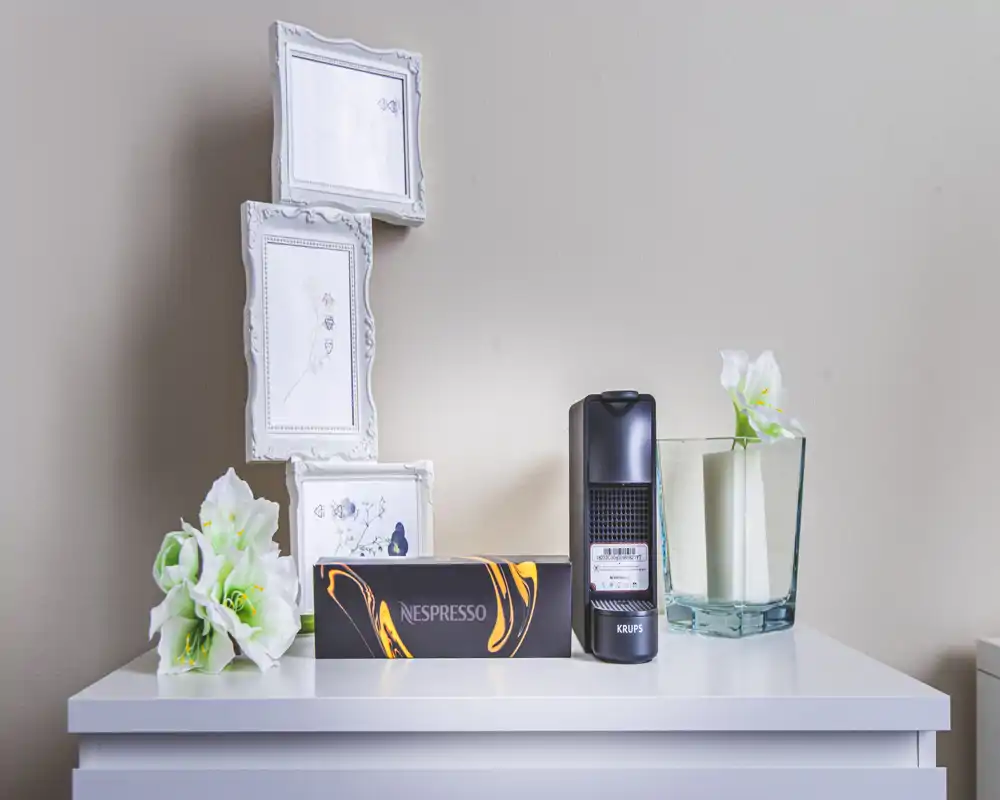 Coin café compact avec machine Nespresso, boîte de capsules et fleurs décoratives sur un meuble blanc — lumineux, propre et adapté à une kitchenette ou un coin café.