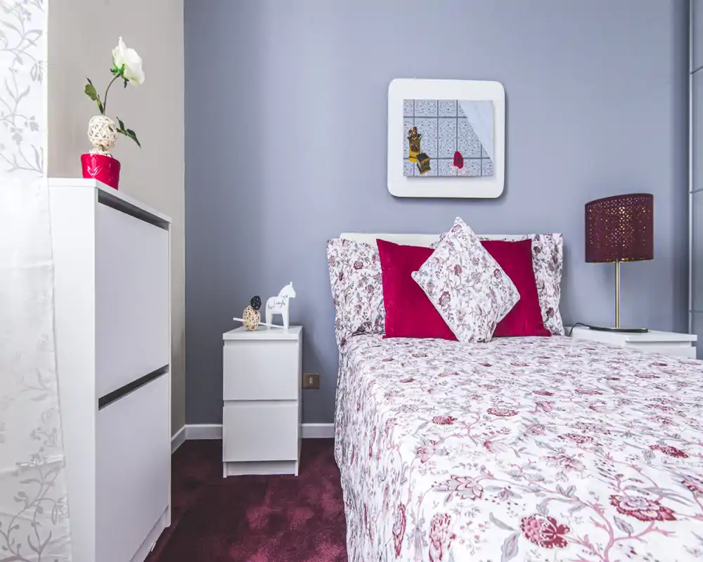 Chambre double lumineuse et soignée avec literie fleurie, coussins décoratifs et tapis coordonné — idéale pour une annonce accueillante.