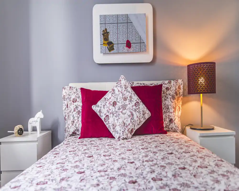 Chambre lumineuse et soignée avec linge de lit à motif et coussins décoratifs; lampe de chevet chaude et tables de nuit symétriques pour une ambiance chaleureuse.