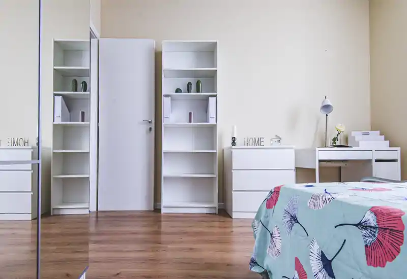 Dormitorio luminoso y minimalista con edredón estampado, muebles blancos y un pequeño escritorio; suelos de madera y detalles decorativos crean un ambiente moderno y tranquilo, perfecto para anuncios.