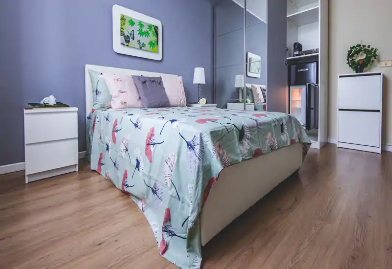 Dormitorio luminoso y bien decorado con una cama grande, ropa de cama con estampado y un armario con espejo que amplía la sensación de espacio.