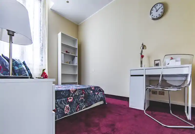 Bright, well-styled single bedroom with patterned bedcover, shelving and a desk — ideal for a student or single occupant.