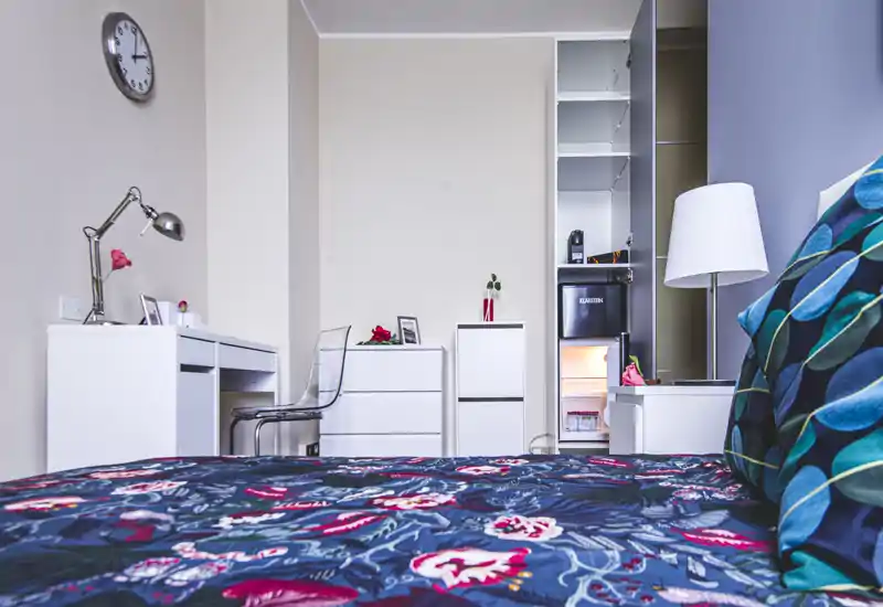 Bright, well-styled bedroom featuring a patterned bedspread, bedside lamp and a small desk area — ideal for a comfortable stay with workspace.
