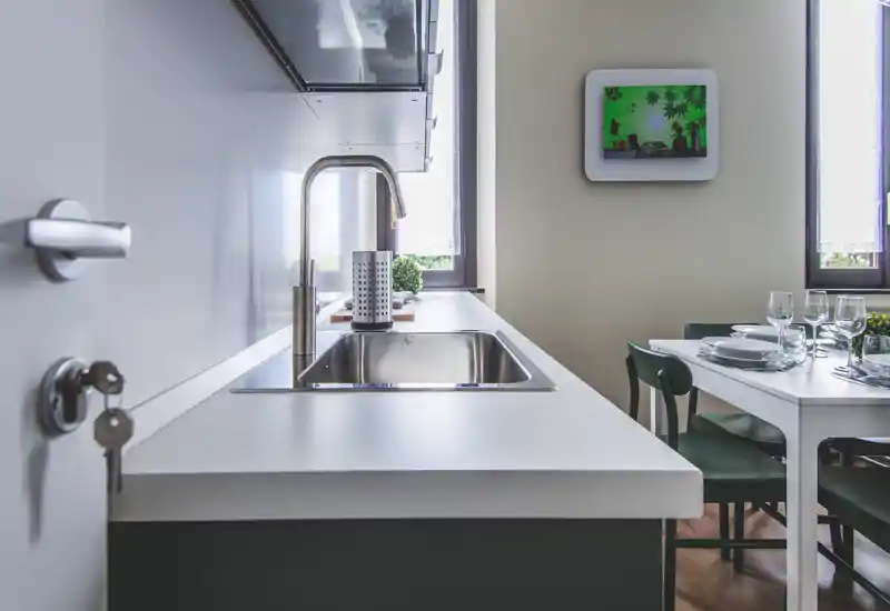 Modern kitchen with a stainless-steel sink integrated into a clean white countertop; adjacent dining table set for a meal and natural light from windows create a bright, inviting space.