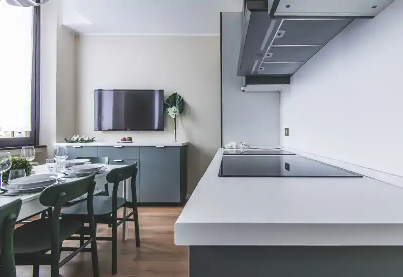 Modern open kitchen with a sleek induction cooktop, white countertops and a small dining area set with tableware — bright, clean and styled for guests.