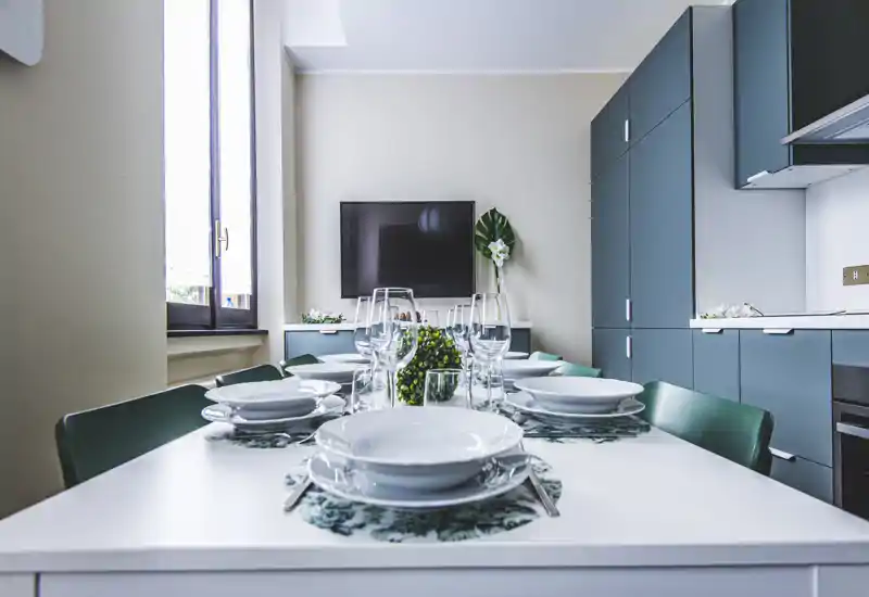 Stylish dining area with a neatly set table, elegant glassware and coordinated cabinetry; bright natural light and modern design create an inviting space for meals.
