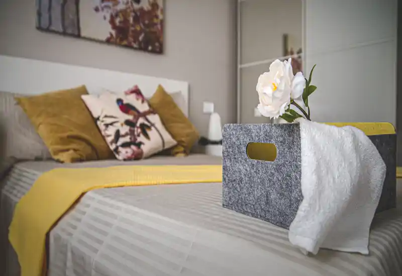 Styled bedroom with a neatly made bed, decorative cushions and a soft yellow throw — bright, cozy and well-staged for rental photos.