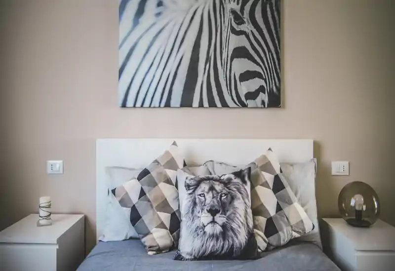 Camera da letto elegante e accogliente con cuscini a motivo, un cuscino decorativo con leone e comodini bilanciati; toni neutri e un quadro che creano un'atmosfera rilassante.