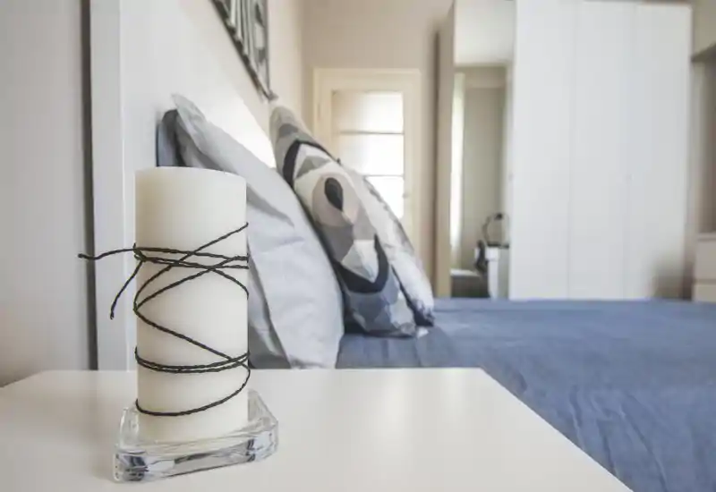Bright, stylish bedroom with a neatly made double bed, decorative pillows and soft blue linens; a candle on the bedside table adds a cozy touch.