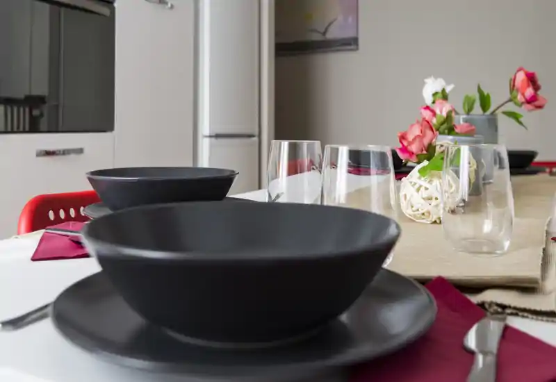 Table dressée avec bols noirs, verres et centre de table floral sur une table lumineuse — un coin repas moderne et accueillant, idéal pour les photos d'annonce.