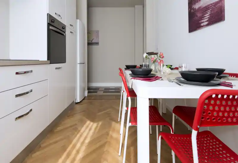Cuisine moderne et lumineuse avec des meubles blancs et une table dressée entourée de chaises rouges — parfaite pour un coin repas compact.