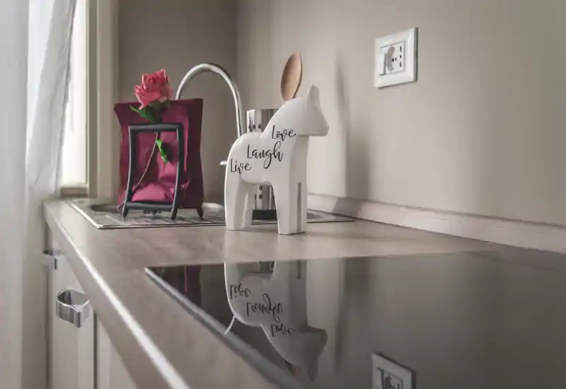 Plan de travail de kitchenette moderne et lumineux avec plaque à induction, figurine décorative et petit évier près de la fenêtre — un espace de préparation soigné et accueillant.