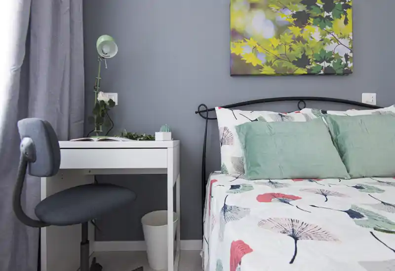 Bright, modern bedroom corner with a patterned duvet, mint-green cushions and a small white desk beside the bed — ideal for a single occupant or short stays.