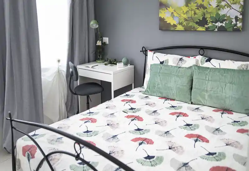 Bright, well-styled bedroom with a patterned bedspread, green cushions and a small desk by the window — ideal for restful nights and light work.