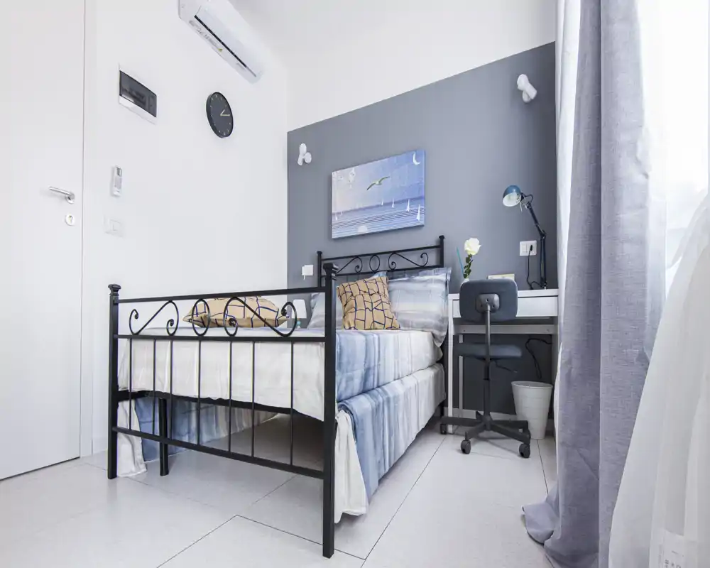 Chambre lumineuse et soignée avec un lit en métal décoratif, des textiles thème bord de mer et un petit bureau à côté de la fenêtre — idéale pour une personne seule ou un étudiant.