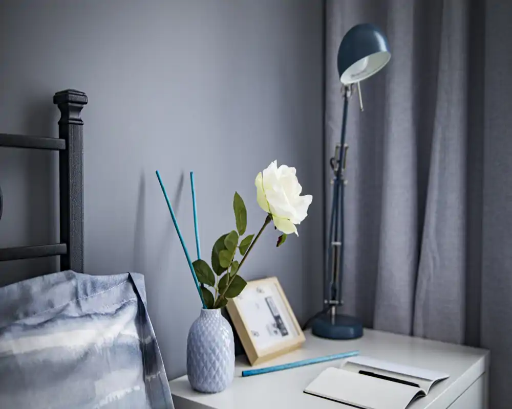 Coin chambre élégant avec tête de lit visible, table de chevet, vase décoratif avec une rose blanche et lampe de bureau — photo lumineuse, moderne et chaleureuse, parfaite pour les annonces.