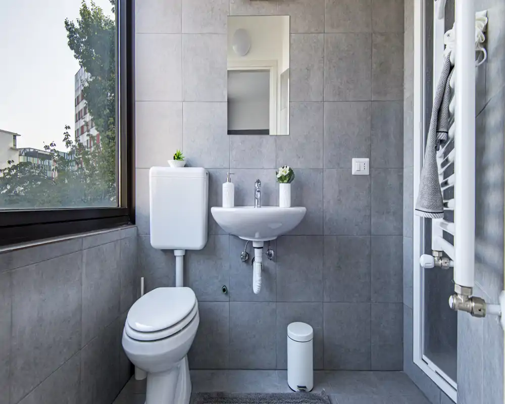 Compact modern bathroom with gray tiles, a wall-mounted sink, toilet, heated towel rail and a large frosted window providing natural light.