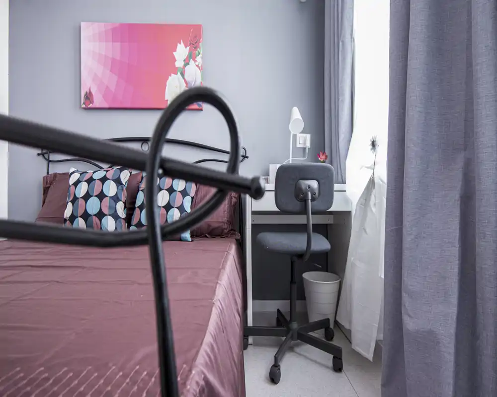 Bright, modern bedroom with a double bed, patterned cushions and a small workspace by the window. Neutral grey walls and coordinated textiles create a calm, contemporary atmosphere.