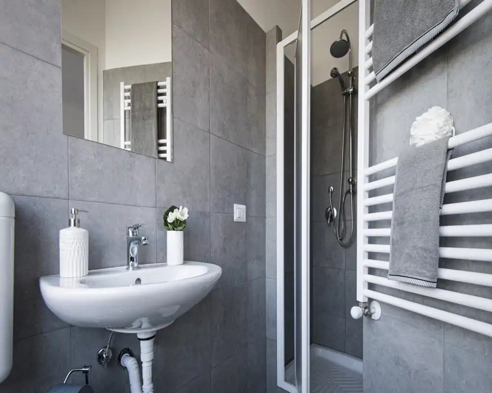 Modern compact bathroom with a wall-mounted sink, a shower enclosure and heated towel rail. Clean gray tiles and minimalist accessories create a neat, functional space.