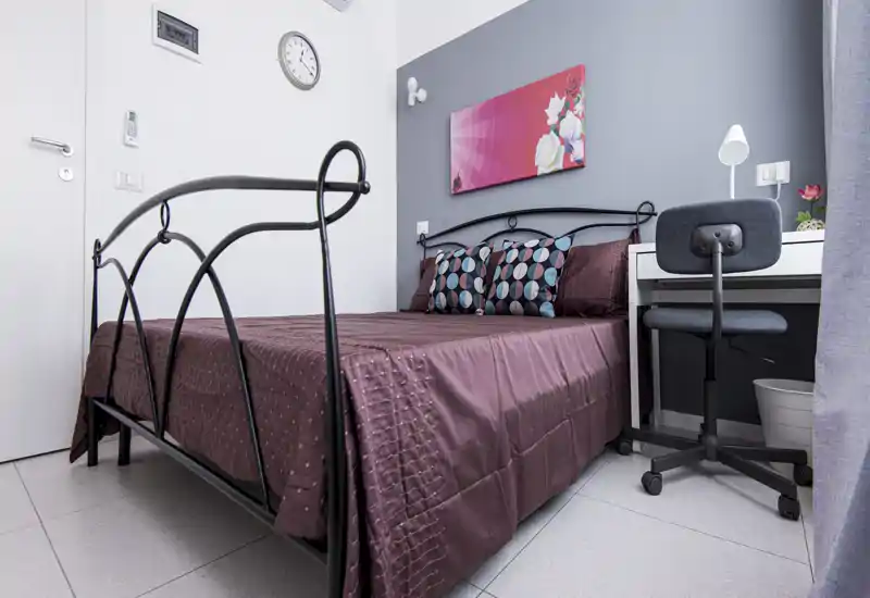 Bright, neatly styled bedroom with a metal-framed double bed, patterned cushions and a small desk — ideal for single travelers or a couple.