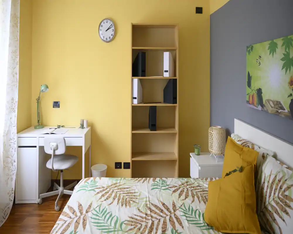 Dormitorio luminoso y moderno con ropa de cama de motivos botánicos, mesita de noche y pequeño escritorio junto a la ventana — acogedor y bien presentado para un anuncio.