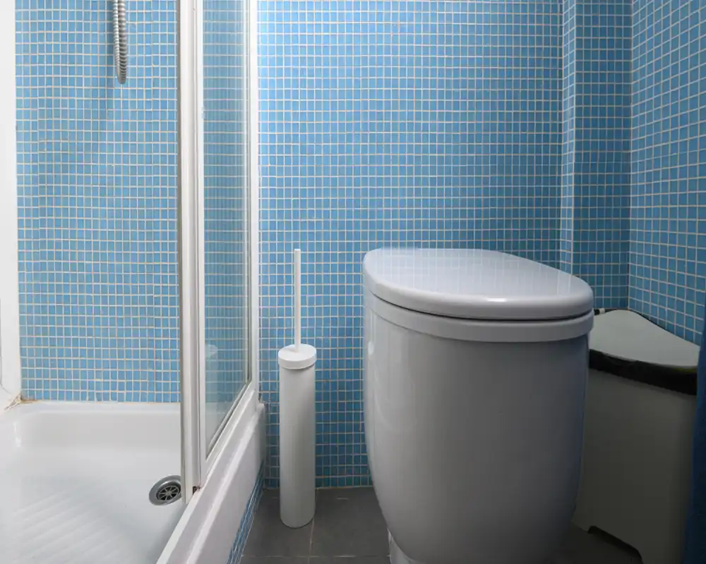 Baño compacto y moderno con azulejos de mosaico azul, inodoro y ducha en esquina. Espacio limpio y bien iluminado, ideal para un apartamento pequeño o baño de invitados.