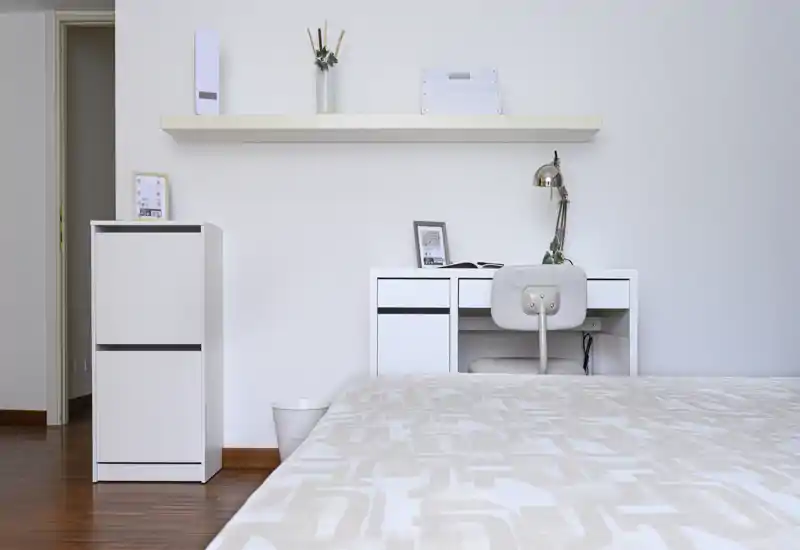 Dormitorio minimalista y luminoso con la cama en primer plano, escritorio blanco y estantería: estética limpia de estilo nórdico.