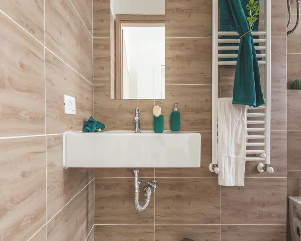 Modern bathroom with wood-effect tiles, a wall-mounted rectangular sink, mirror and heated towel rail with teal accessories.
