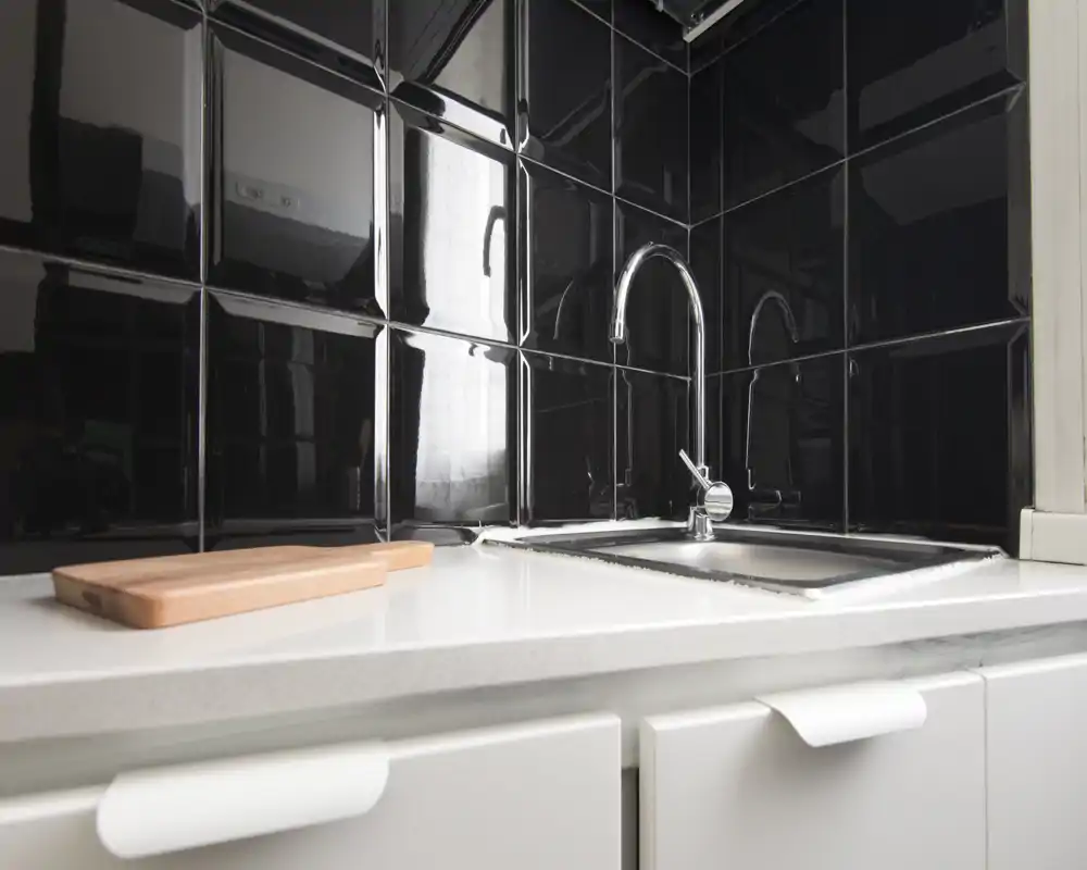 Compact modern kitchen countertop with a stainless-steel sink, chrome faucet and glossy black tile backsplash; a wooden cutting board adds a warm accent.