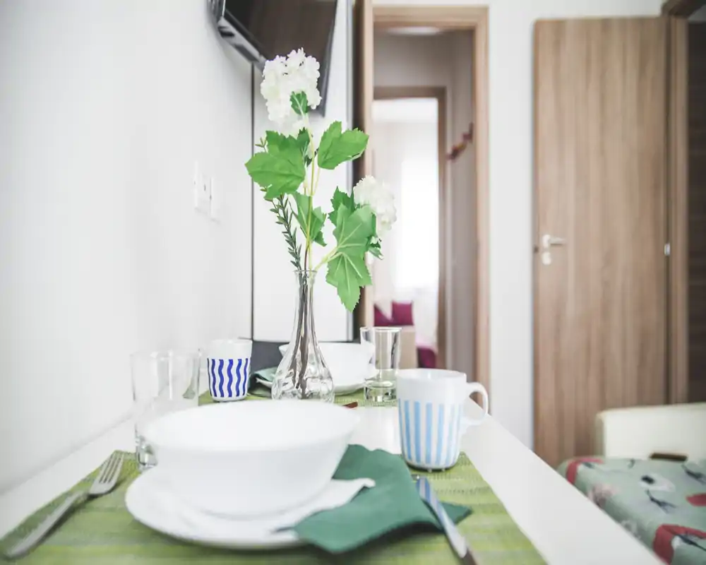 A bright, set dining surface with plates, mugs and a vase of flowers; compact dining area visible in a modern interior with a doorway leading to another room.