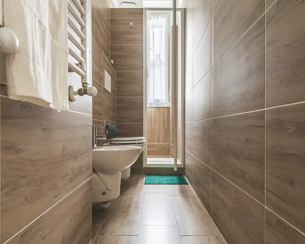 Bright, modern bathroom with wood-effect tiles, wall-mounted toilet and bidet, and a small shower area at the far end.