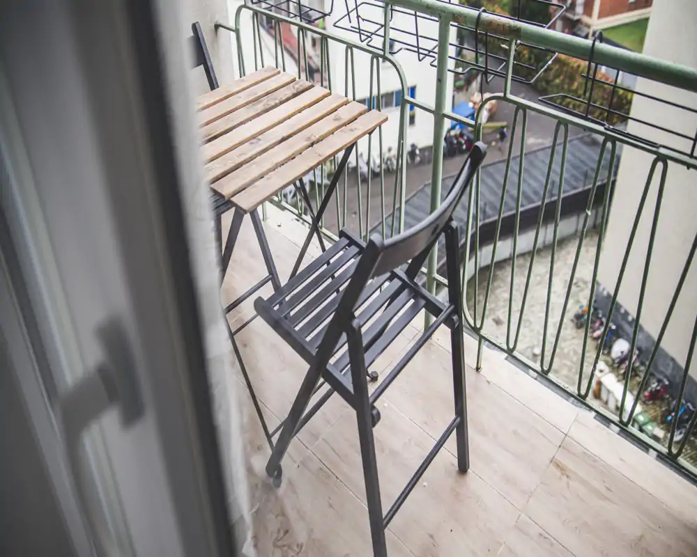 Small private balcony with a wooden folding table and a metal chair, overlooking a courtyard — ideal for morning coffee.