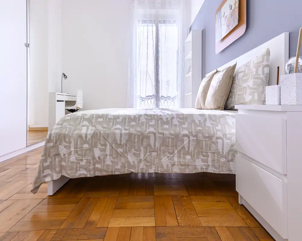 Bright, modern bedroom with a large bed framed by soft linens, bedside table and natural light from a window, ideal for a cozy rental listing.