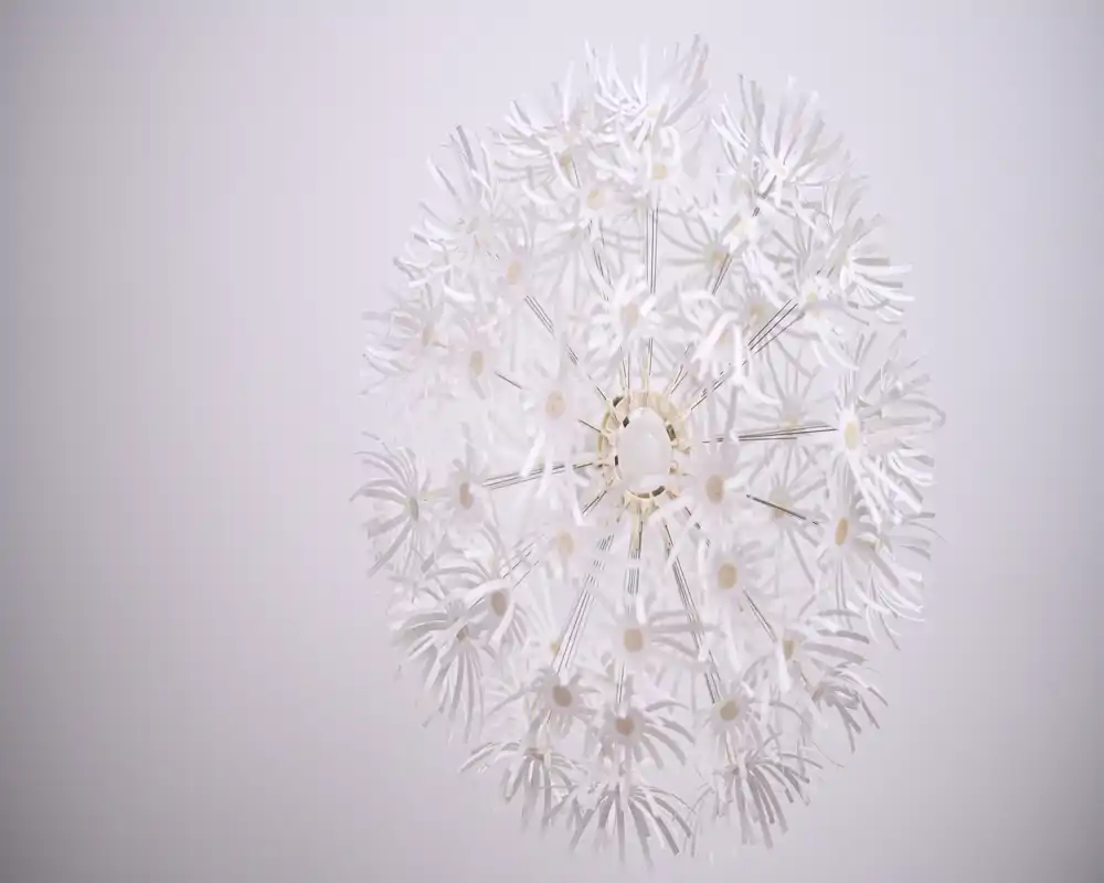 Plano cercano de una lámpara decorativa esférica contra un techo claro. Los elementos en forma de pétalo forman una figura parecida a un diente de león, creando un detalle moderno y delicado.