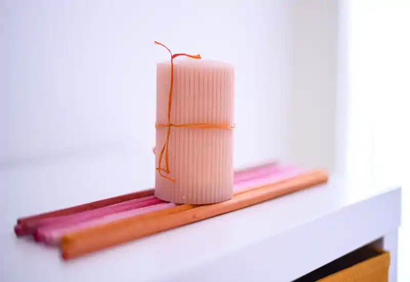 Primer plano de una vela decorativa sobre una superficie blanca con palitos de colores — una imagen de detalle para producto o decoración, no muestra una habitación completa.
