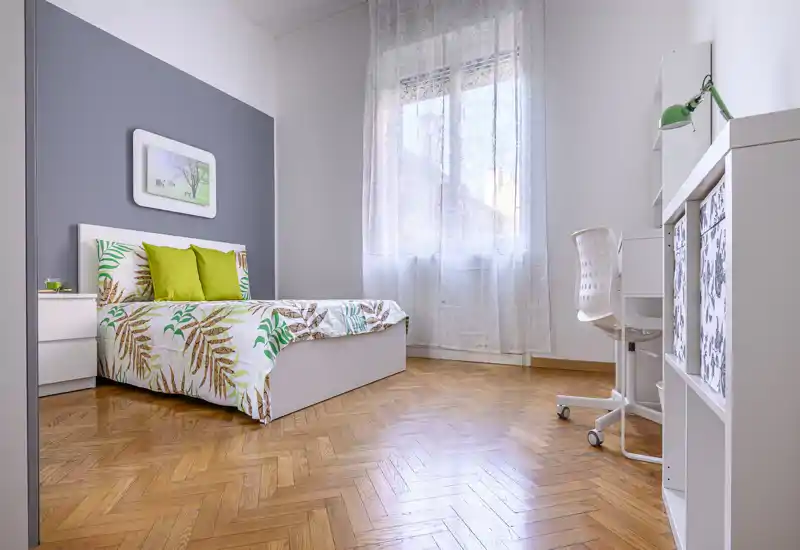Habitación individual luminosa y moderna con suelo de parquet, ropa de cama estampada y una zona de escritorio acogedora junto a la ventana — ideal para estudiante o profesional.