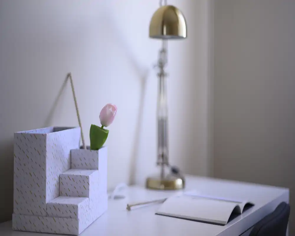 Un angolo scrivania minimalista e ordinato con un tulipano decorativo, una lampada dorata e un taccuino aperto — ideale per un piccolo spazio di lavoro domestico o come composizione per un comodino.