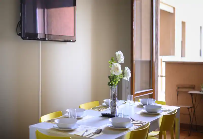 Table à manger lumineuse dressée pour six avec des chaises jaunes modernes et un centre de table floral, ouverte sur la lumière naturelle d'une porte-fenêtre.