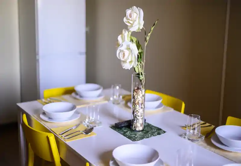 Coin repas stylé avec une table dressée pour quatre, chaises jaunes vives et un élégant centre de table floral — idéal pour des repas conviviaux et des photos attrayantes.