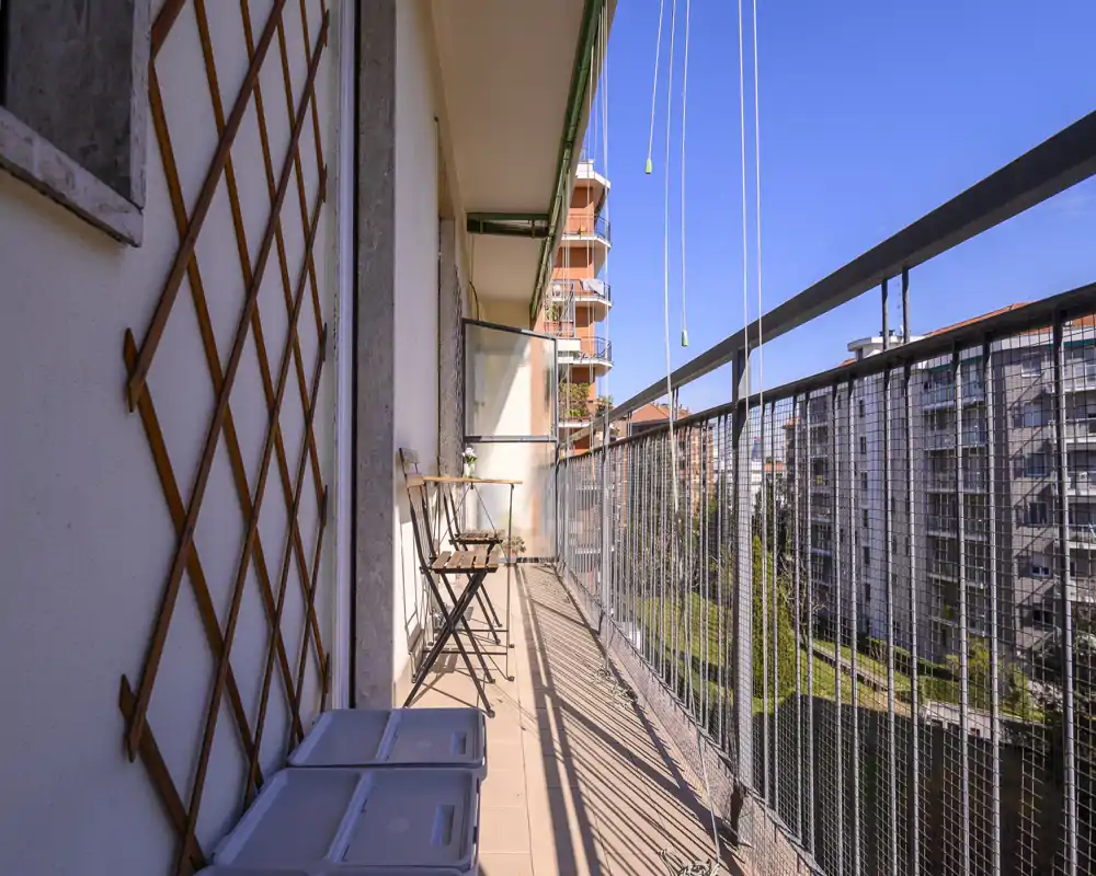 Sunny narrow balcony with metal railing, small bistro table and chairs — ideal for morning coffee with an urban view.