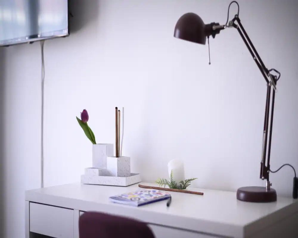 Bright, minimal desk corner with a lamp, decorative tulip and candle — ideal for a calm workspace inside the living area.