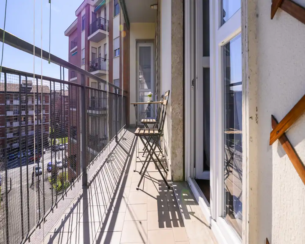 Sunny narrow balcony with two folding chairs and a small table, overlooking neighboring apartment buildings — ideal for a morning coffee.
