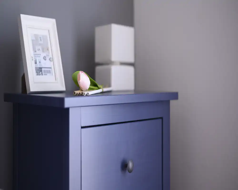 Close-up detail of a blue chest or bedside table with a framed photo, decorative cubes and a single tulip; the shot focuses on the furniture detail rather than showing the full room.