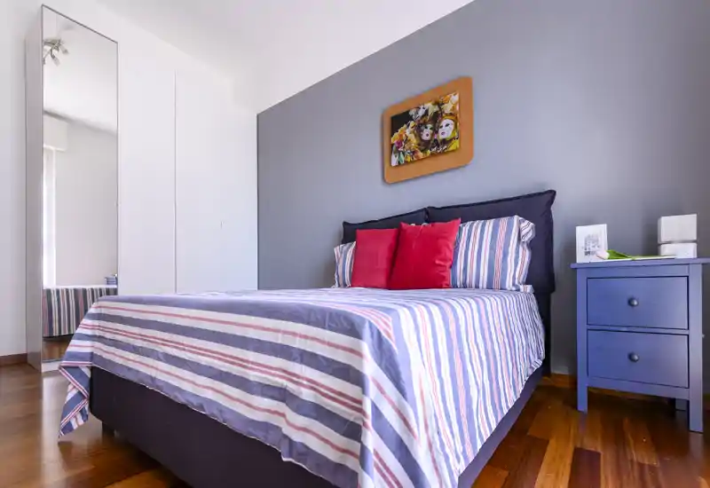 Dormitorio luminoso y bien presentado con cama a rayas, cojines coloridos y mesita de noche — acogedor y listo para invitados.