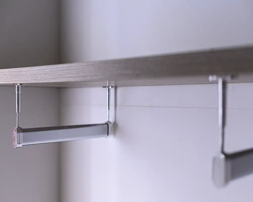 Close-up of a wardrobe/closet hanging rail and shelf bracket; minimal context for the surrounding room.